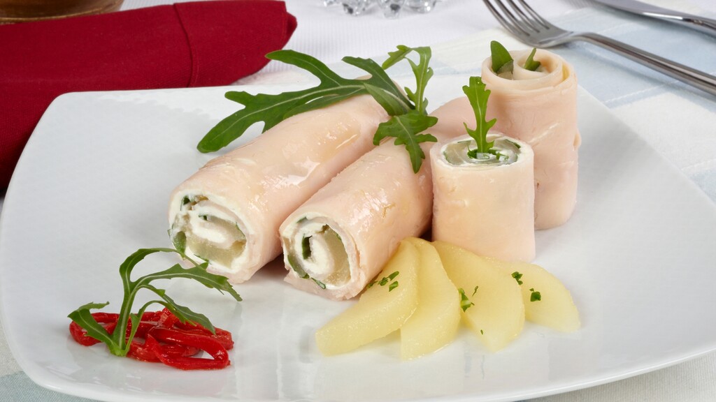 Turkey and cheese roll-ups served on a white plate with greens.