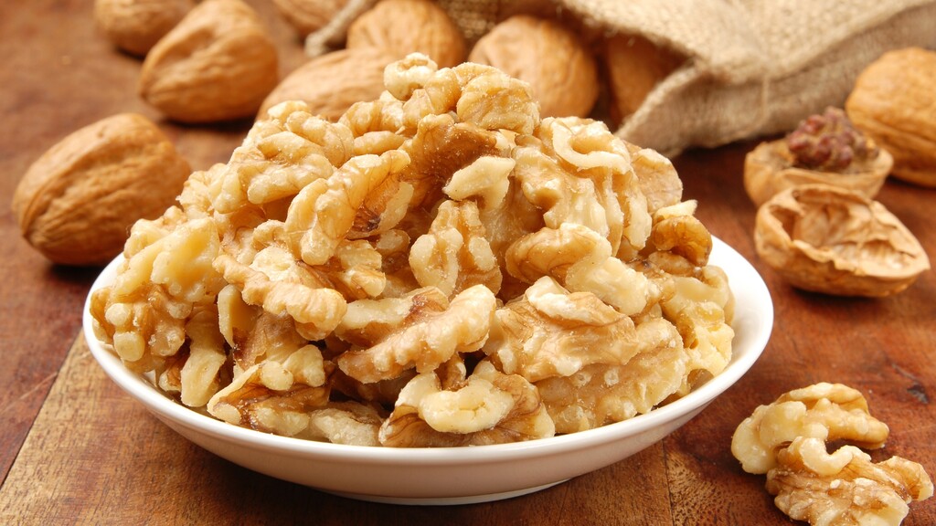 Walnut halves in a white bowl with whole walnuts on a wooden table.