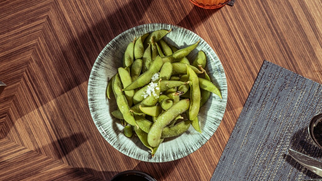 Steamed edamame pods with coarse salt in a small bowl.
