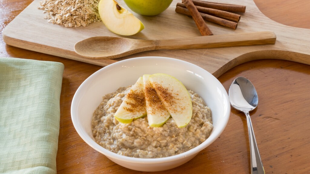 A bowl of cooked oatmeal topped with apple slices and cinnamon.