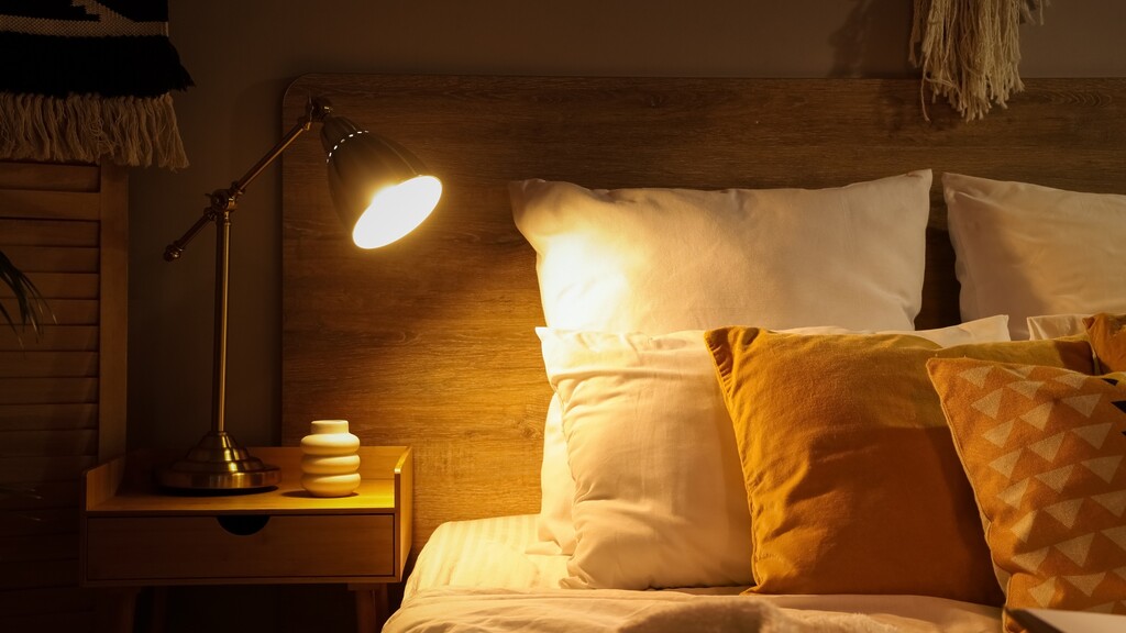 Cozy bedroom with an amber bedside lamp, pillows, and a calm sleep environment.