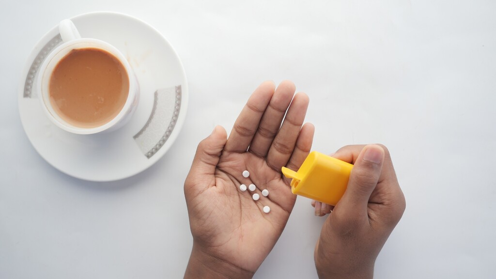 Hands pouring artificial sweetener tablets beside a cup of coffee, illustrating a common habit that may affect gut health.