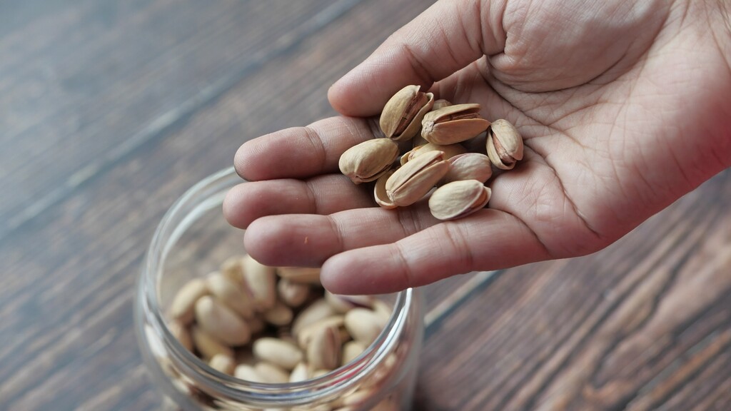 A small handful of in-shell pistachios held over a glass jar.