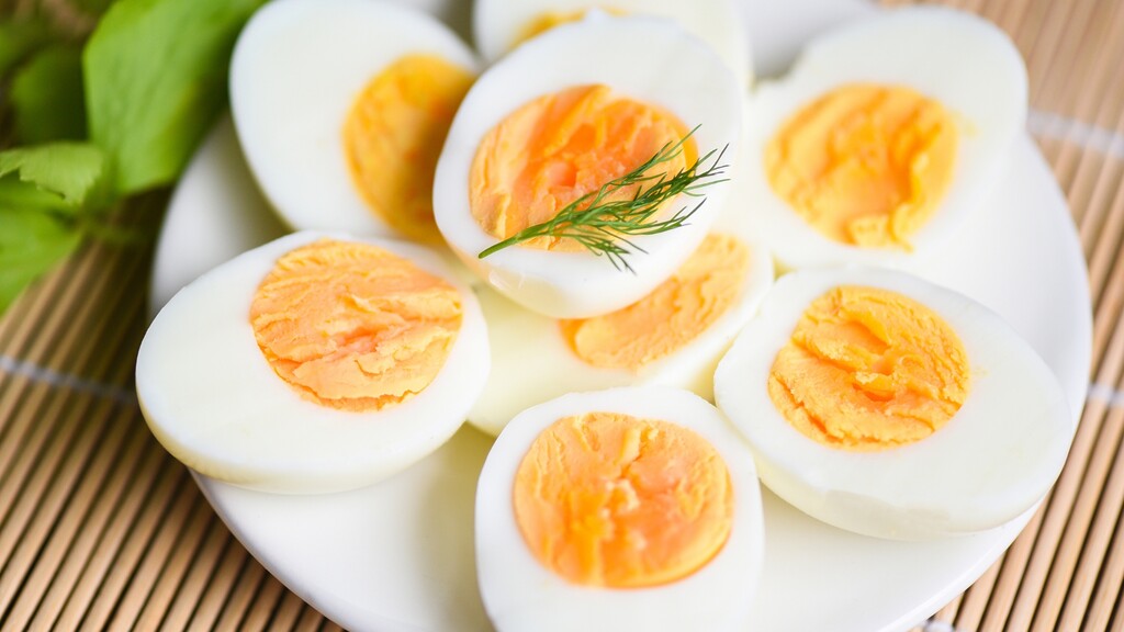 Sliced hard-boiled eggs served on a white plate with fresh herbs.