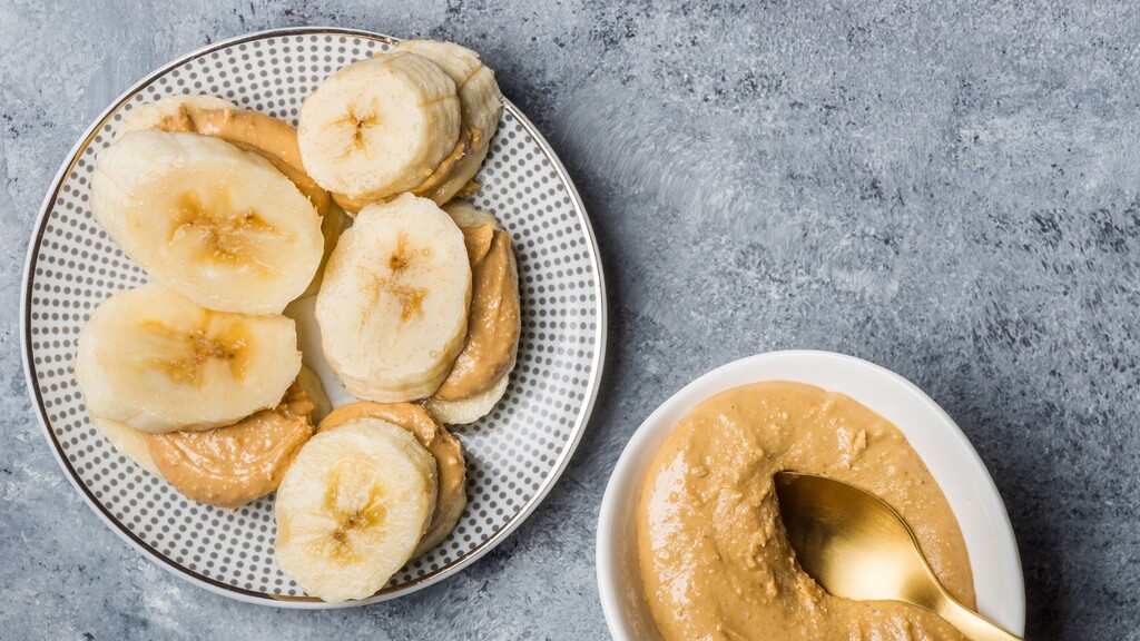 Banana slices topped with almond butter beside a small bowl of nut butter.