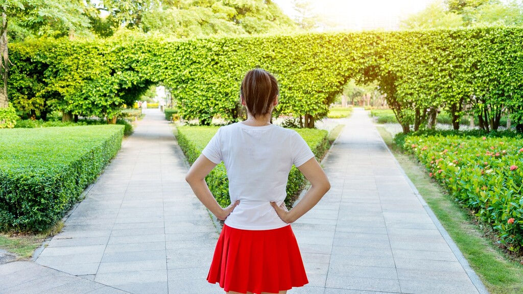 Woman standing at a forked garden path, symbolizing the choice to break old generational parenting patterns.