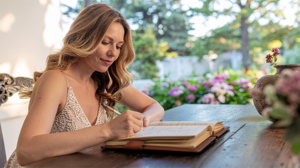 Woman writing in a journal at an outdoor table, reflecting on parenting patterns and emotional triggers.