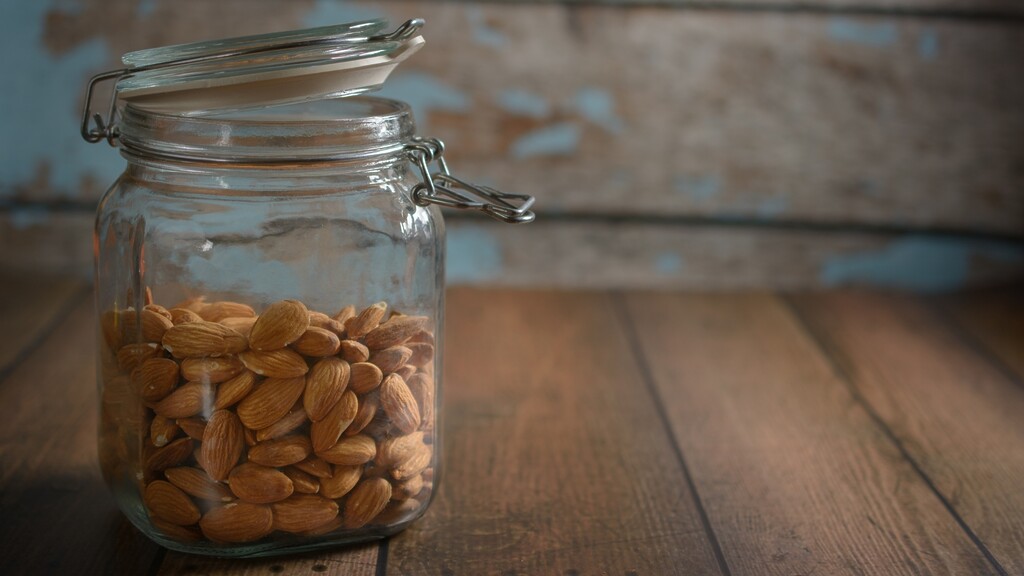 Raw almonds stored in a glass jar on a wooden surface.