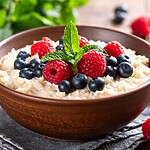 Bowl of oatmeal topped with raspberries, blueberries, and fresh mint.