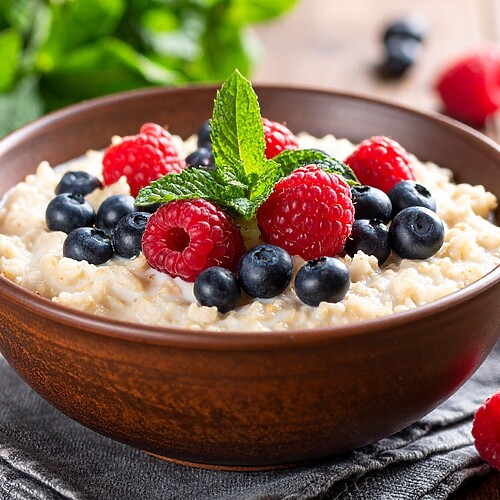 Bowl of oatmeal topped with raspberries, blueberries, and fresh mint.