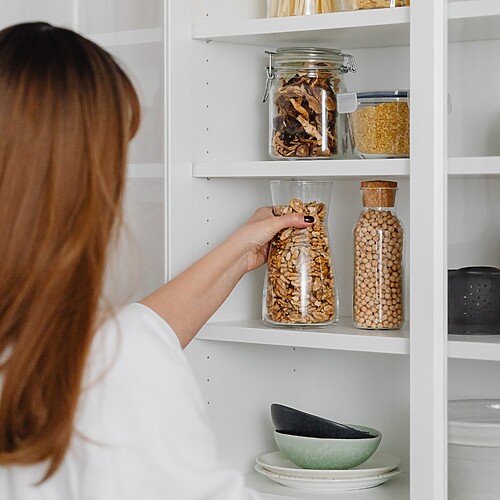 Woman organizing glass jars of nuts, legumes, and dry goods on a clean pantry shelf.
