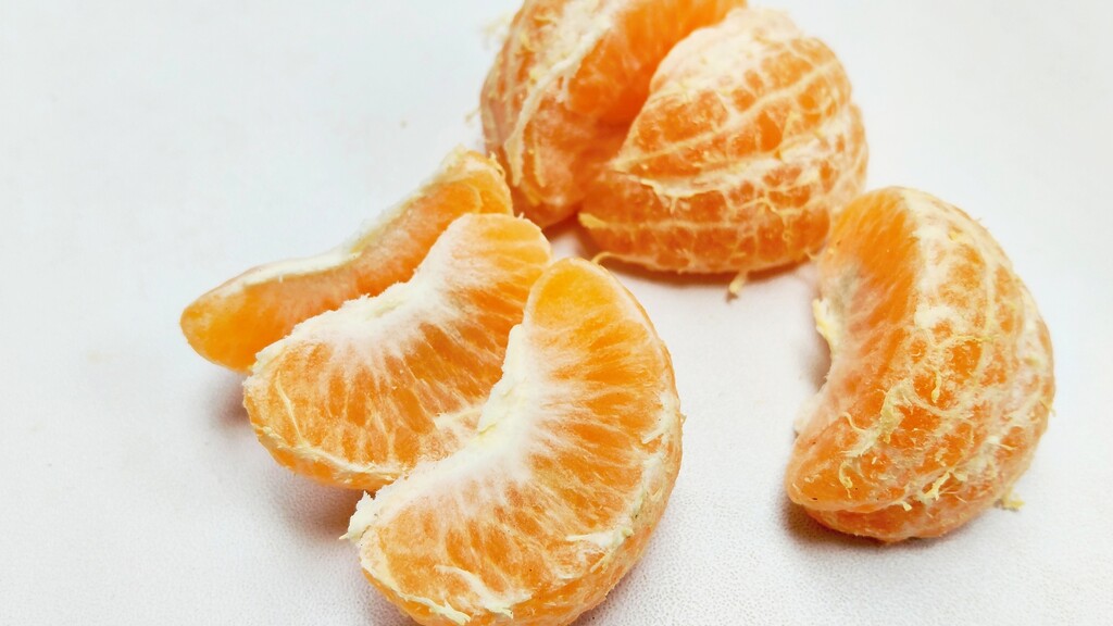 Peeled orange segments with white pith still attached on a light surface.