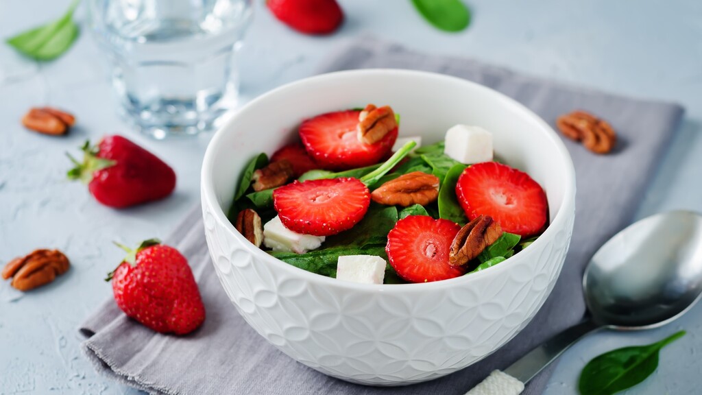 Strawberry spinach salad with pecans and cheese in a white bowl.