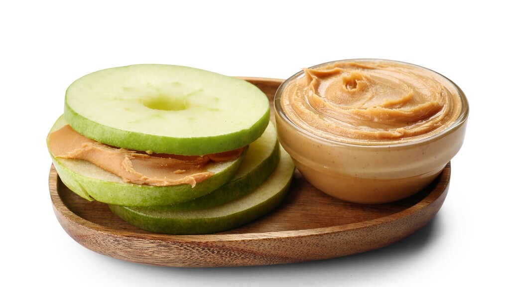 Green apple slices with peanut butter on a wooden plate.