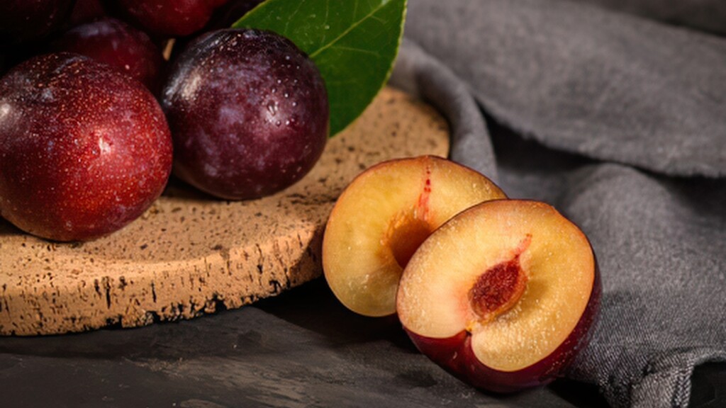 Fresh plums, including one sliced open to show the yellow flesh.