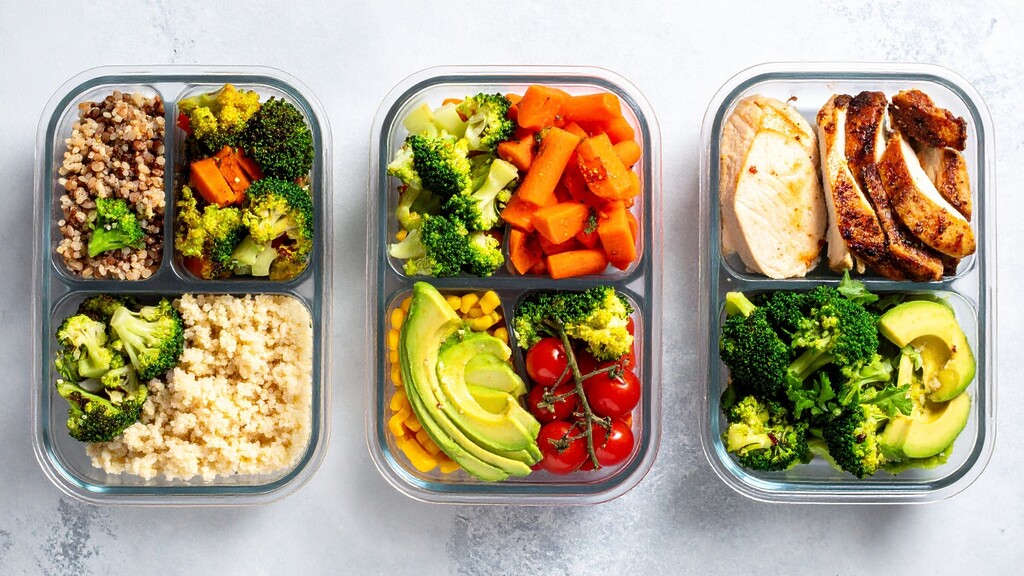 Three glass meal prep containers filled with chicken, avocado, broccoli, tomatoes, and prepared vegetables. 