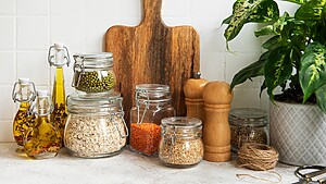 Organized pantry counter with glass jars of grains, legumes, infused oils, and a wooden cutting board.