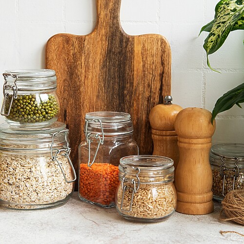 Organized pantry counter with glass jars of grains, legumes, infused oils, and a wooden cutting board.