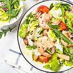 Shrimp salad with leafy greens, tomatoes, and lemon wedges in a ceramic bowl.