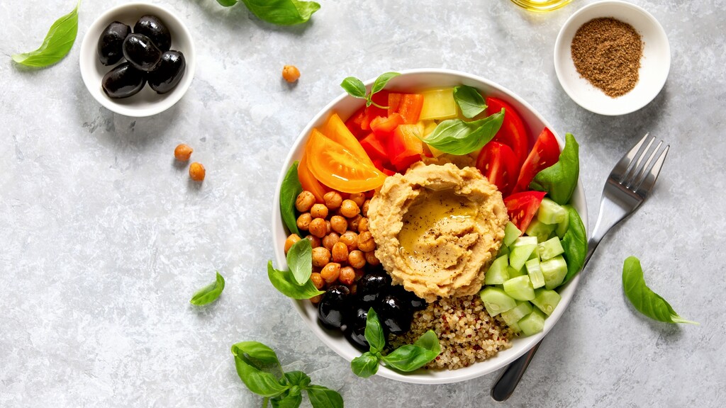 Mediterranean grain bowl with hummus, chickpeas, tomatoes, cucumber, olives, basil, and quinoa.