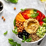 Mediterranean grain bowl with hummus, chickpeas, tomatoes, cucumber, olives, basil, and quinoa.