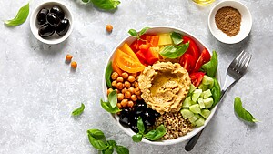Mediterranean grain bowl with hummus, chickpeas, tomatoes, cucumber, olives, basil, and quinoa.