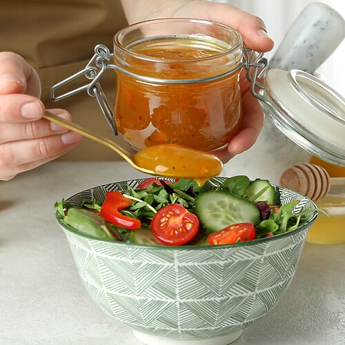 Homemade vinaigrette being spooned over a fresh salad with cucumbers, tomatoes, lemon, and honey.