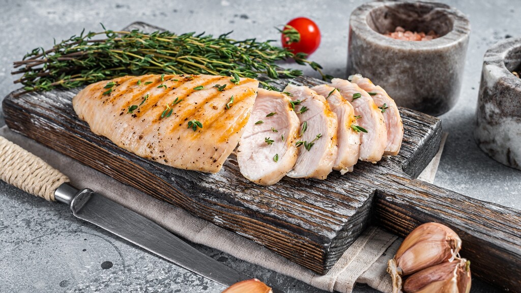 Sliced roasted turkey breast with fresh herbs on a rustic cutting board as a lower-sodium deli meat alternative.