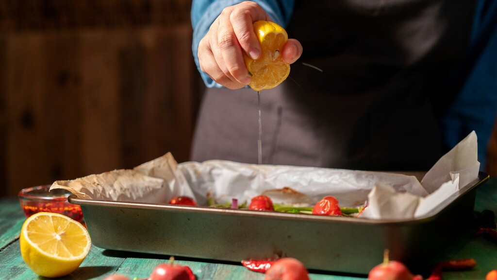 Hand squeezing fresh lemon juice over roasted vegetables in a baking tray.