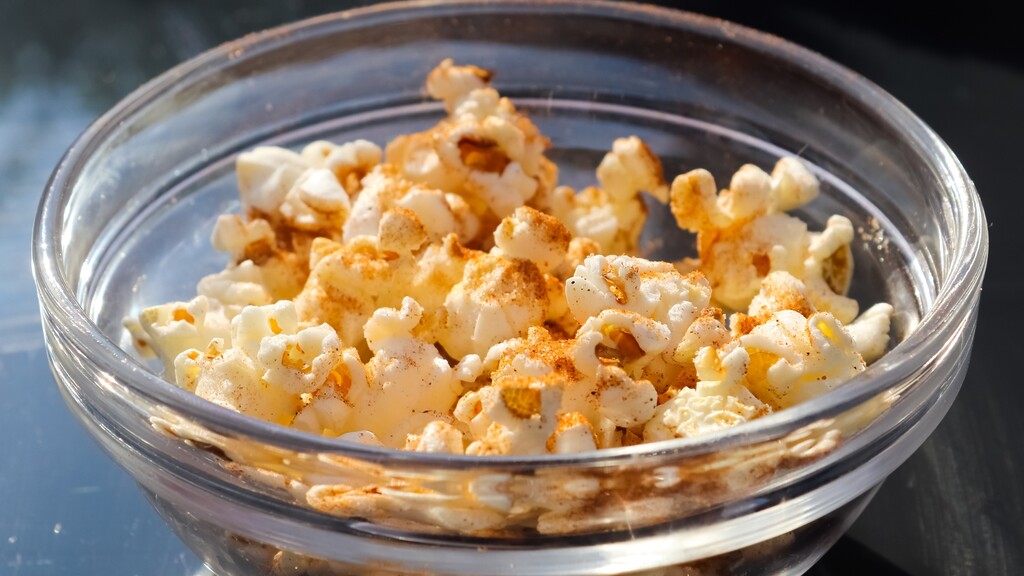 Air-popped popcorn seasoned with paprika in a clear glass bowl as a crunchy low-sodium snack.