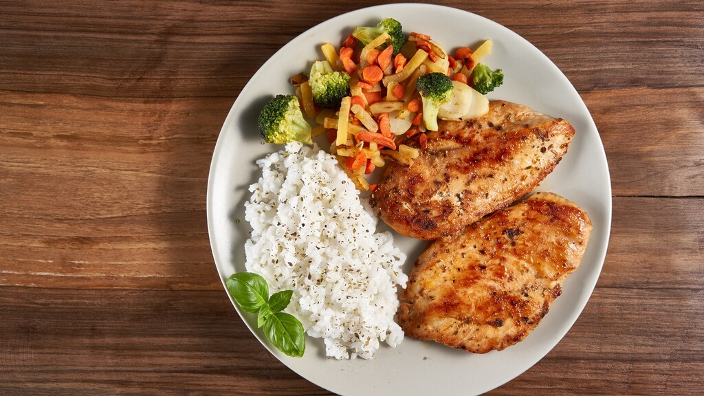 Grilled chicken breast served with white rice and mixed vegetables on a plate, showing a simple balanced meal with protein, carbs, and vegetables.
