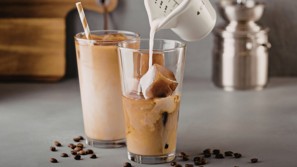 Milk being poured into iced coffee, illustrating a coffee drink made with a healthy-seeming carb source.