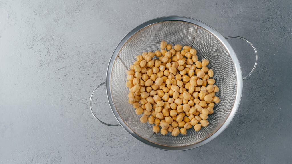 Rinsed chickpeas draining in a metal colander on a gray kitchen surface.
