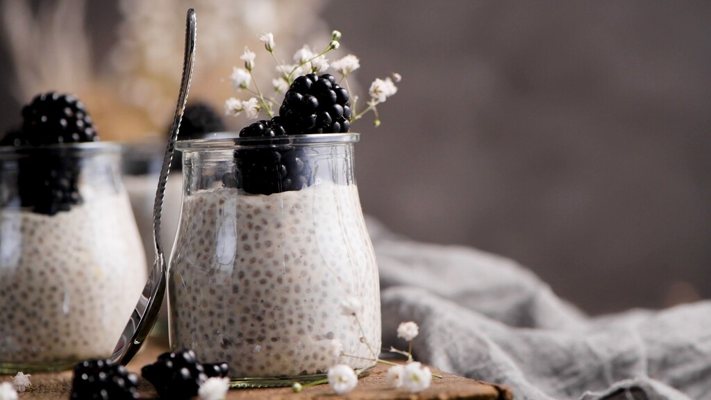 Chia seed pudding in glass jars topped with blackberries on a rustic table.