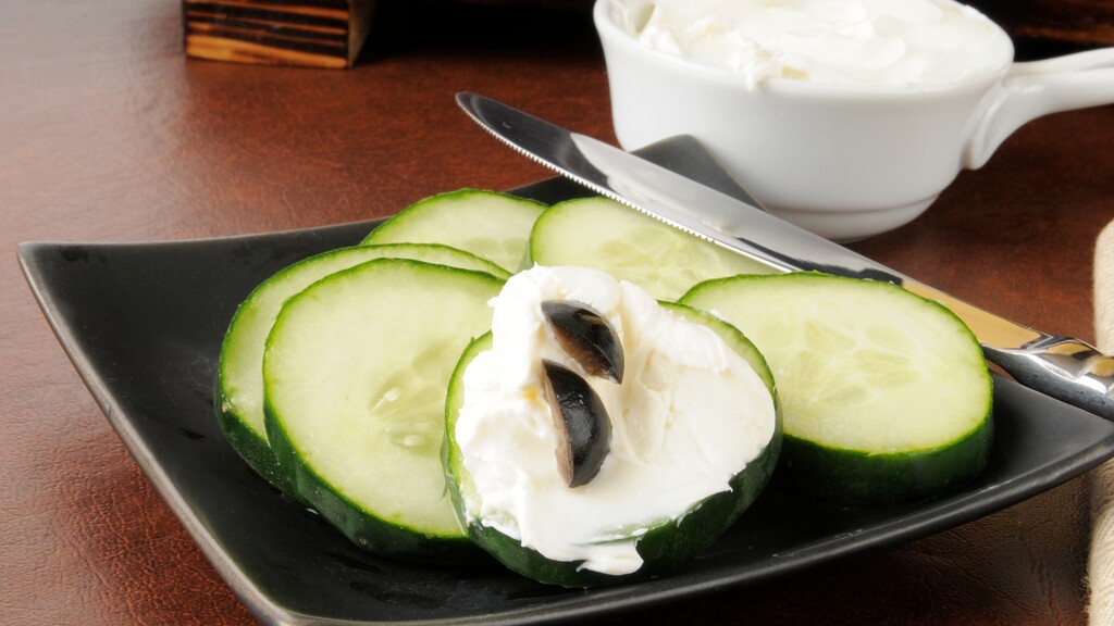 Cucumber slices topped with cream cheese on a black plate as a crunchy low-carb swap for rice cakes.