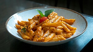 Penne pasta in creamy tomato sauce served in a white bowl with basil and a cherry tomato garnish.