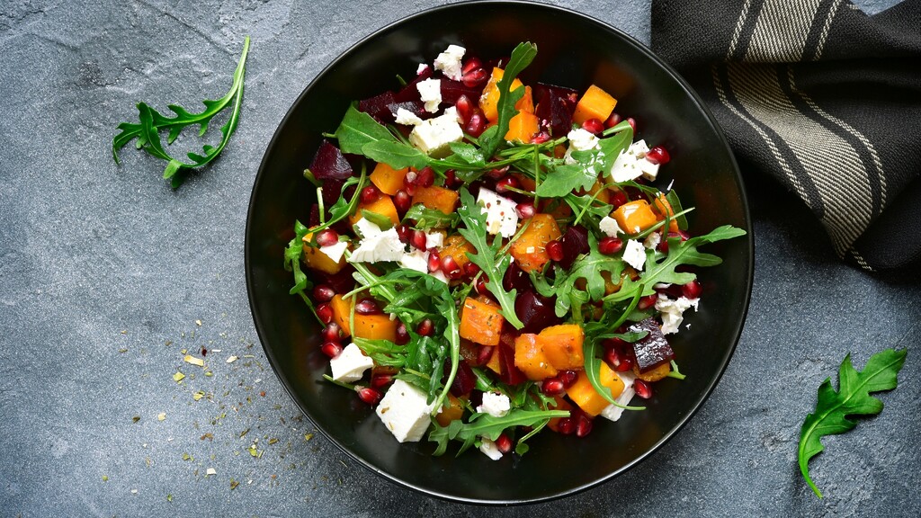 Beet and squash salad with feta, arugula, and pomegranate in a black bowl.