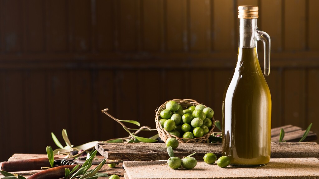 Bottle of olive oil with fresh green olives and olive branches on a rustic wooden surface.
