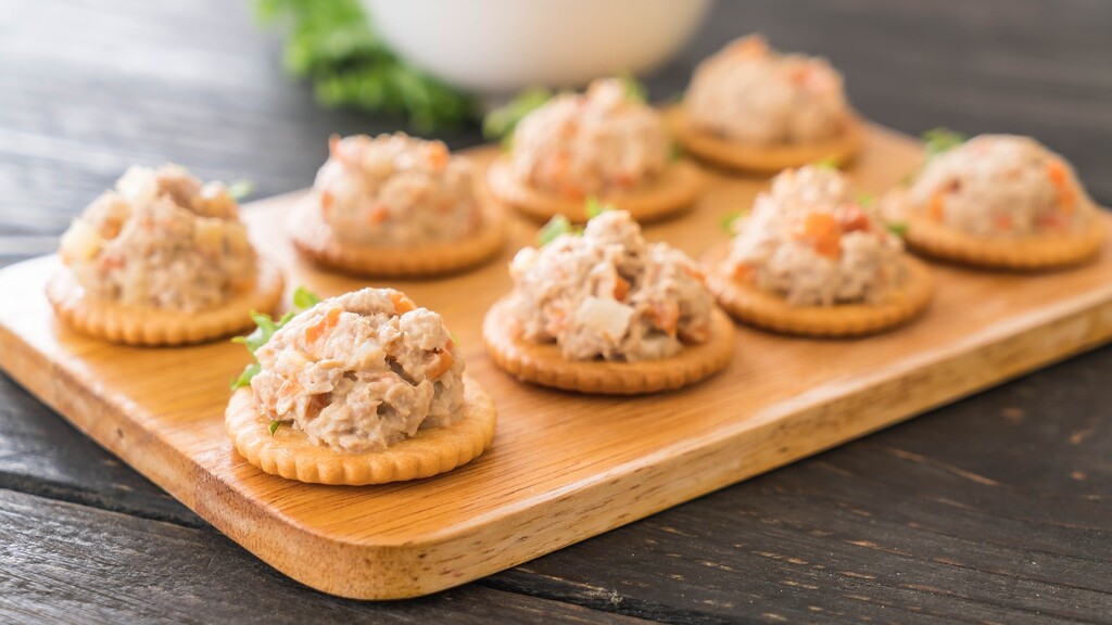 Tuna salad served on round crackers on a wooden board.