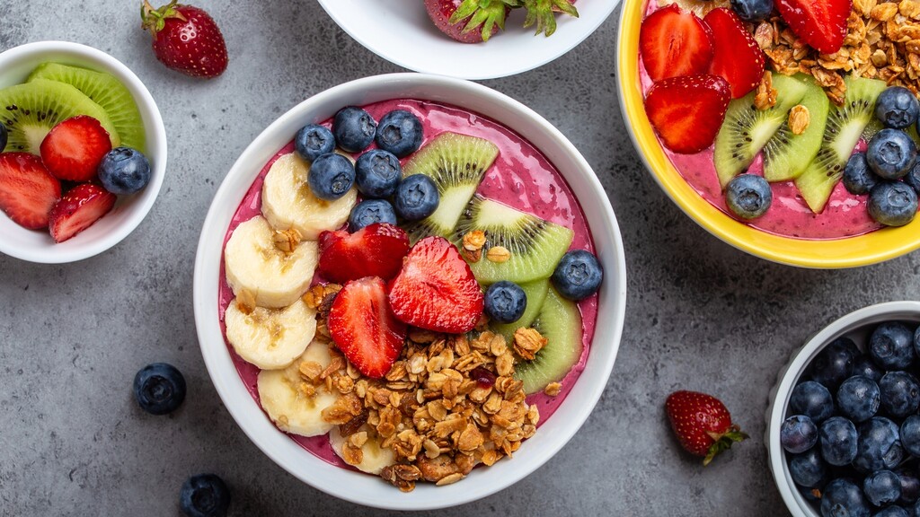 Smoothie bowls topped with strawberries, kiwi, blueberries, banana, and granola.