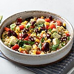 Quinoa salad with kidney beans, corn, avocado, red peppers, herbs, and lime wedges in a ceramic bowl.