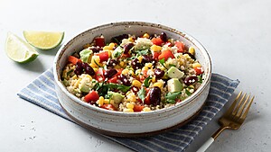 Quinoa salad with kidney beans, corn, avocado, red peppers, herbs, and lime wedges in a ceramic bowl.