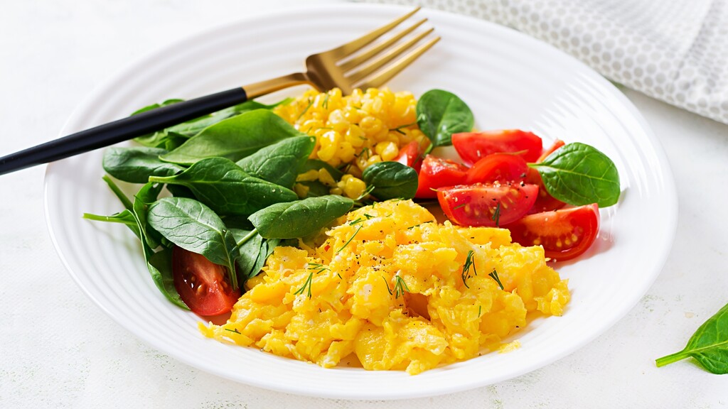 Scrambled eggs served with spinach, tomatoes, corn, and herbs for a savory vegetable breakfast.