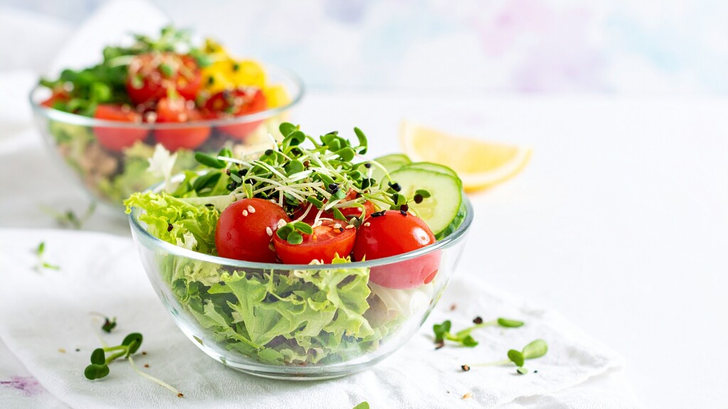 Fresh Mediterranean salad with lettuce, tomatoes, cucumber, sprouts, and lemon wedges.