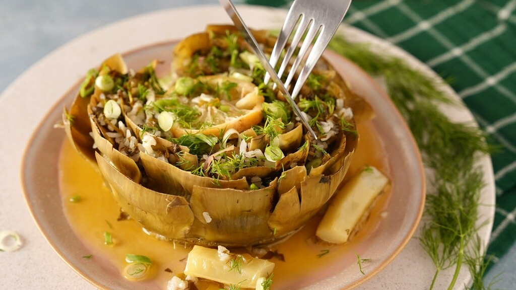 Stuffed artichoke with rice, herbs, lemon, and broth served on a ceramic plate.