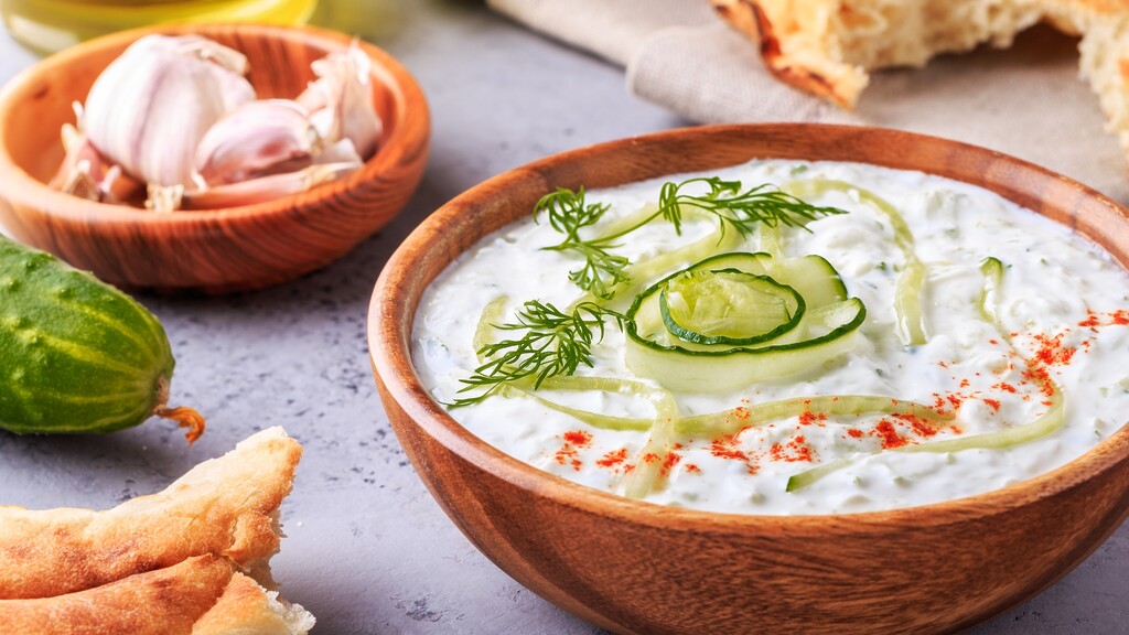 Savory Greek yogurt cucumber sauce with garlic, herbs, and bread on a rustic table.