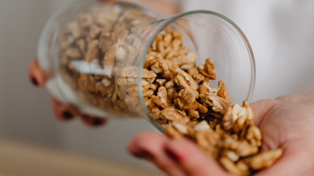 Walnuts being poured from a glass jar into a hand, showing a simple healthy Mediterranean snack ingredient.