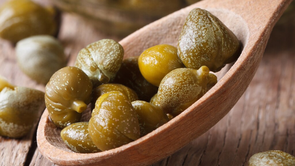 Close-up of capers on a wooden spoon, showing a salty Mediterranean ingredient used to add bright flavor to dishes.