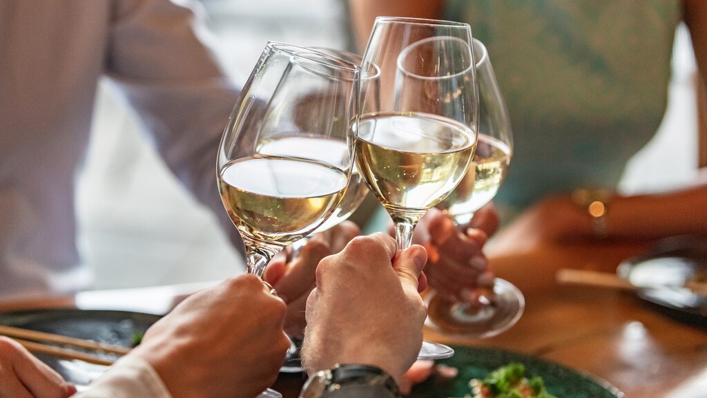 Friends clinking glasses of dry white wine over a Mediterranean-style meal.