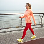 Woman walking outdoors on a waterfront path in athletic clothes during a low-impact fitness workout.